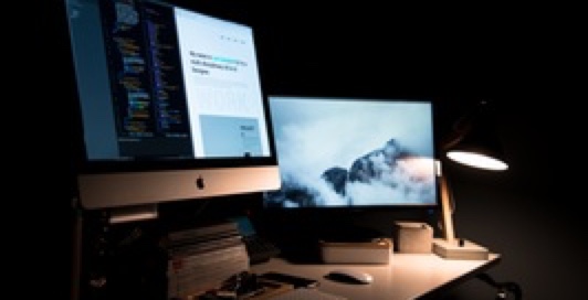 Picture of a iMac and monitor on a desk in a dark room