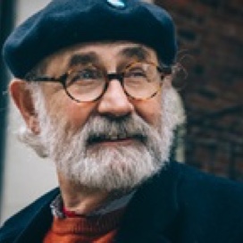 Picture of a man with a grey beard, glasses and a beret looking to the right